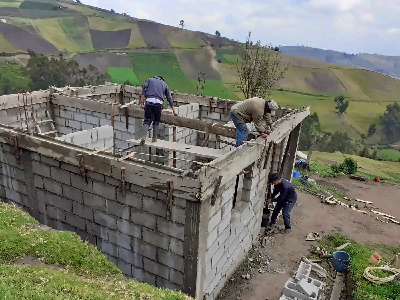 Tre uomini al lavoro sulle casseforme di una casa in blocchi di cemento