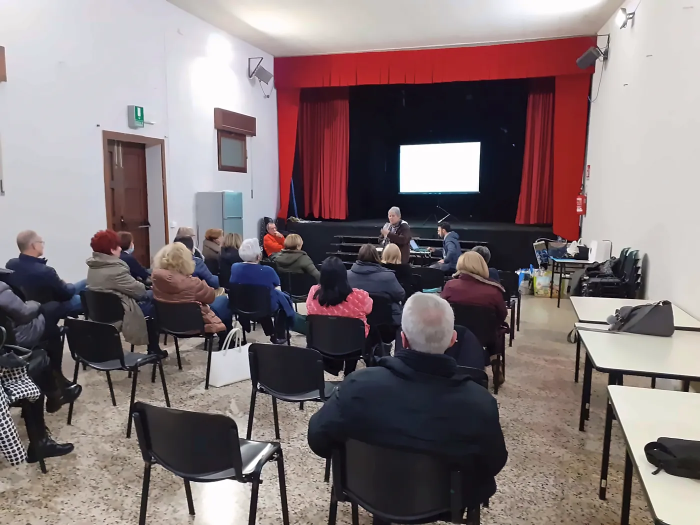Incontro con i sostenitori in una sala parrocchiale, con proiezione sul palco