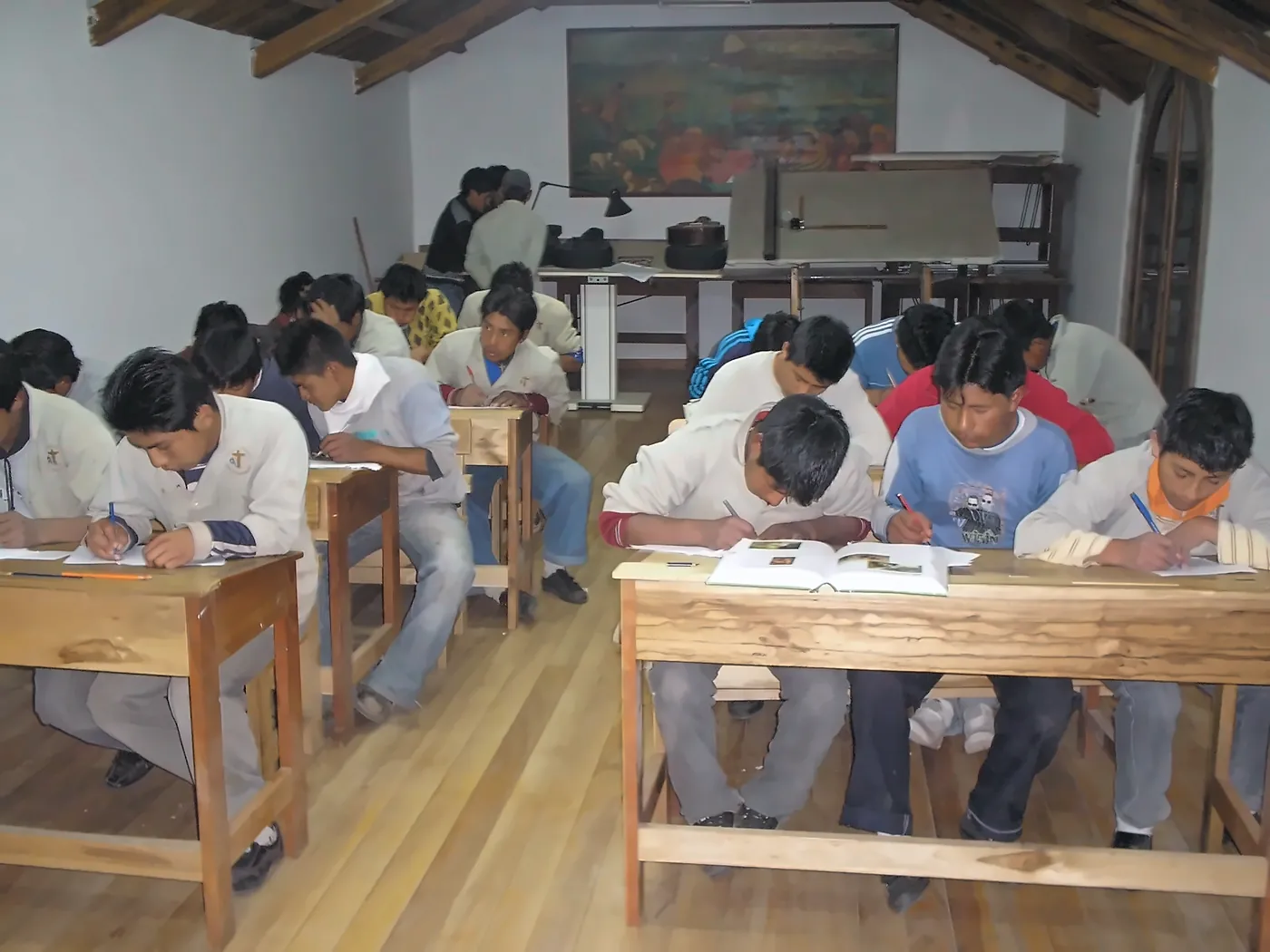 Ragazzi in camice seduti ai banchi di legno durante una lezione di disegno