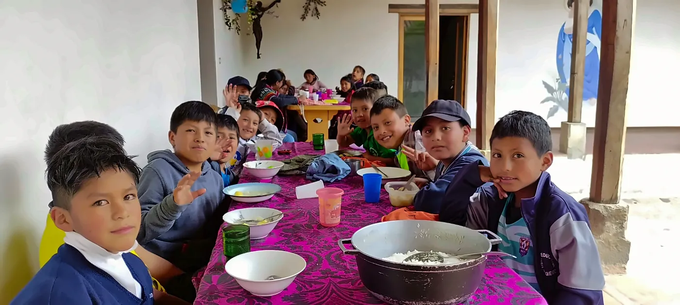 Bambini seduti a una lunga tavola apparecchiata che salutano verso la fotocamera