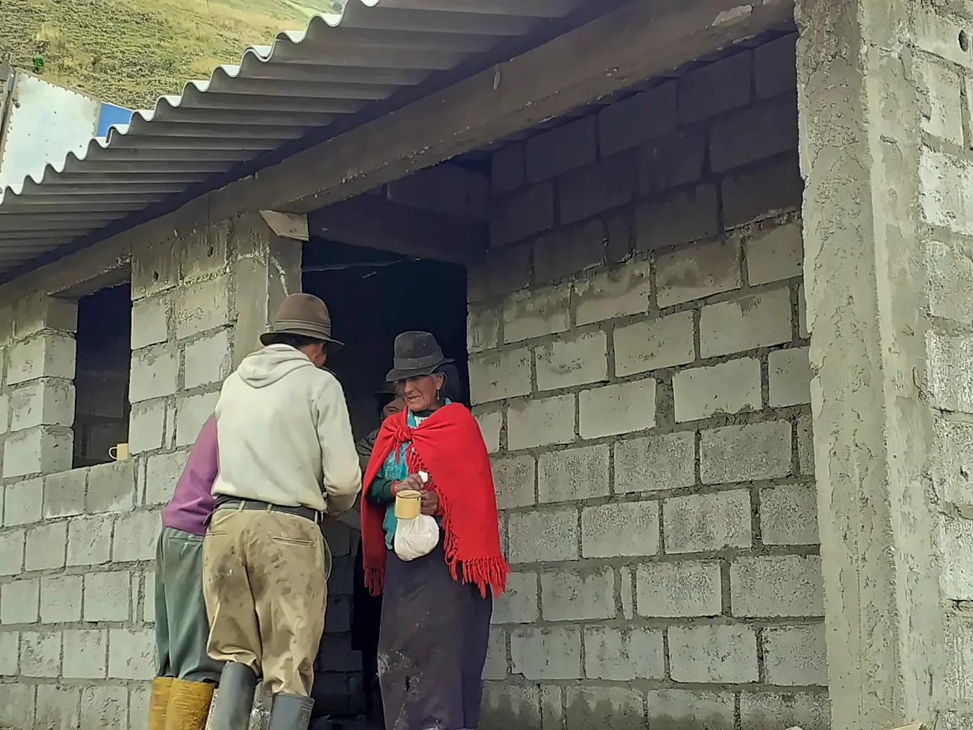 Una donna con poncho rosso offre da bere ai lavoratori davanti alla nuova casa in costruzione